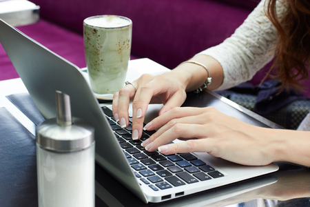 Cropped view of young female office worker sitting at table in cafe enjoying coffee and surfing internet after hard day at work.の写真素材