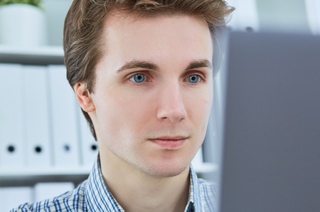 Young employee looking at computer monitor during working day in office.