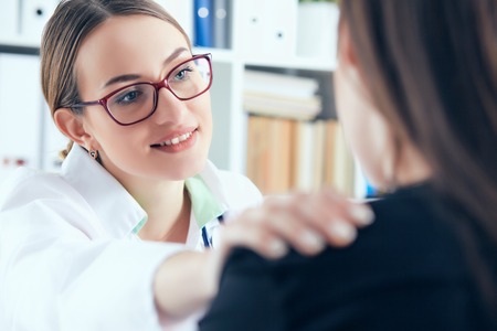 Friendly female doctor in glasses touching patient shoulder. Encouragement, empathy, cheering and support after medical examination.の写真素材