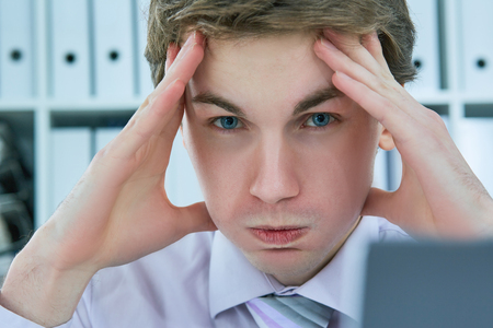 Overworked young businessman having headache after hard working day and touching his head.の写真素材