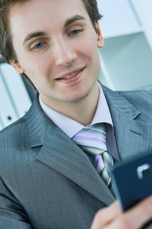Portrait of smiling business man reading message with smartphone in office.の写真素材