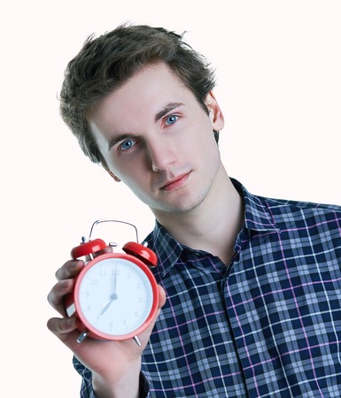 Close-up portrait of a troubled young man holding alarm clock isolated over white background.の写真素材