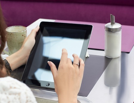 Cropped view of young female office worker sitting at table in cafe enjoying coffee and surfing internet at tablet after hard day at work.の写真素材