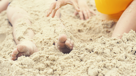 Childrens feet are buried in sand. Happy holiday on th e sea coast.の写真素材