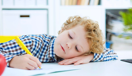 Tired little boy sitting at the table, with hishead on his arm,の写真素材