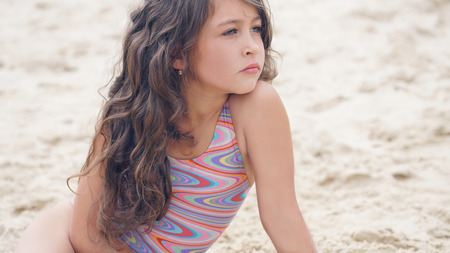 Close-up portrait of a pretty little Hispanic girl with waving in the wind long hair sitting on the beach.の写真素材