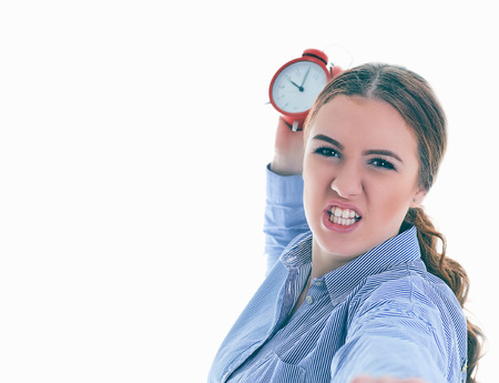Angry young Caucasian woman throwing an alarm clock isolated in white background.の写真素材