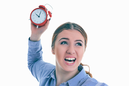 Angry young Caucasian woman throwing an alarm clock isolated in white background.の写真素材