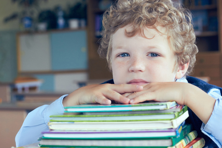 Cute young Caucasian schoolboy lying on top of a pile of books at classroom.の写真素材