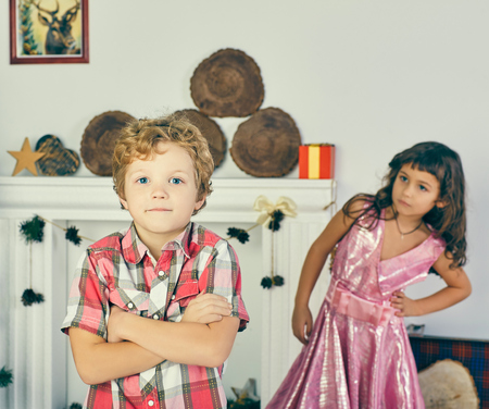 Little cross-armed Caucasian curly boy and girl play and pose indoors.の写真素材