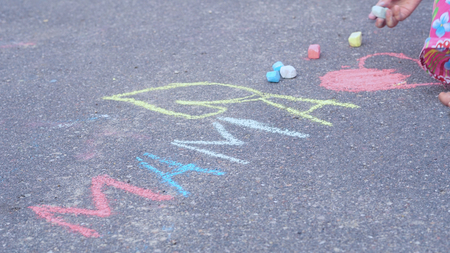 Little girl writes word mama by chalk on the asphalt. Family conceptの写真素材