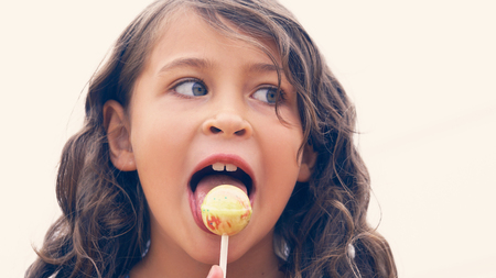 Cute little Latin girl with a colorful candy on tropical beach vacationの写真素材