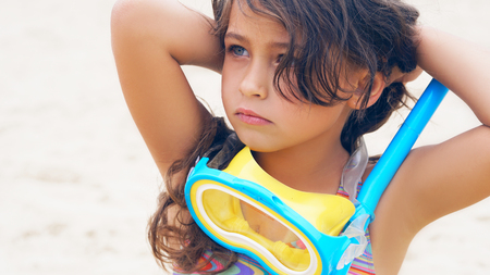 Beautiful little girl playing on the seacoast in mask for swimmingの写真素材
