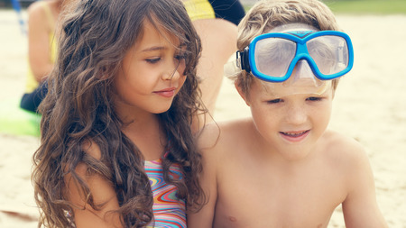 Portrait of children on the beach in summer. Little girl sitting with er frend on the sand and smiling.の写真素材