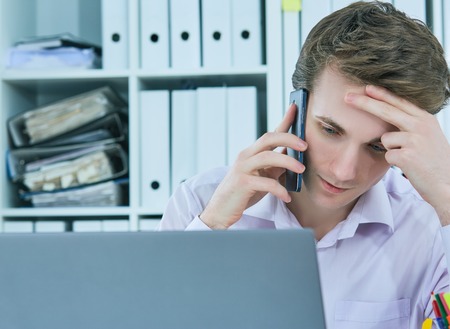 White collar talking to customer on mobile phone in office at workplace by laptop.の写真素材