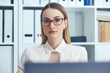 Portrait of young serious businesswoman looking at the camera while using laptop in office.の写真素材