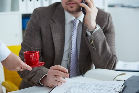 Woman hands giving a cup of coffee to a businessman. Secretary giving coffe to a boss.の写真素材