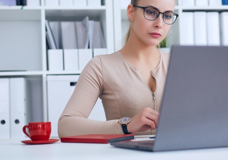 Young beauiful Caucasian businesswoman in glasses working on notebook computer and business document at office.の写真素材