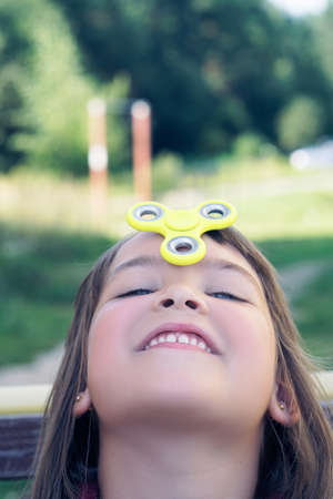 Young caucasian girl play with fidget spinner stress relieving toy on her forehead.の写真素材