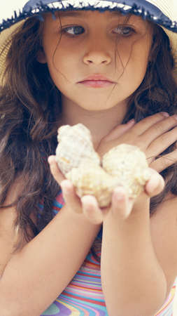 Close up of sad little girl in hat holding sea shells in her hands.