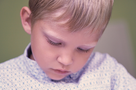 Little Caucasian boy looks at something below while sitting at a table indoor.