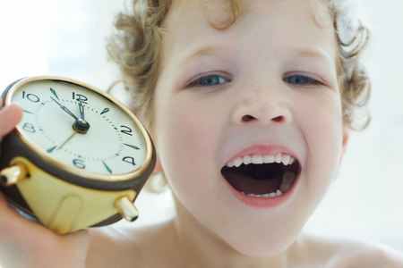 Little Caucasian curly boy yawns holding an antique clock.の写真素材