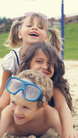Portrait of smiling children lying on the beach in summer. Little girls hugs their brother.の写真素材