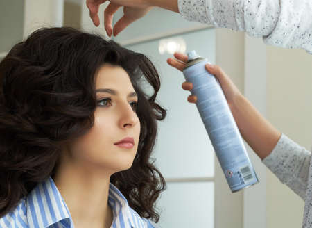 Side view of hairdressers hands using hairspray on clients hair at salon.の写真素材