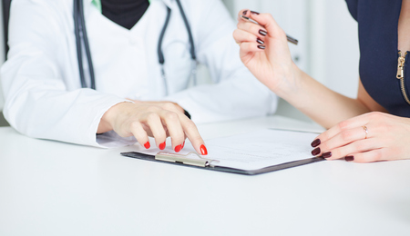 Female patient at reception of doctors office filling out medical form. Just hands over the table.の写真素材