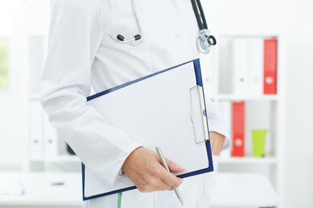 Female medicine doctor holding a clipboard with a blank sheet of paper closeup. Doctor is waiting for patient to examine.の写真素材
