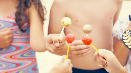 Cute brother and sisters enjoying lollipops outside at the Beach.の写真素材