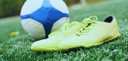 Soccer ball and football boots on green grassの写真素材