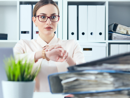 Shocked female manager looking at her watch near a pile of documents. Deadline concept.の写真素材