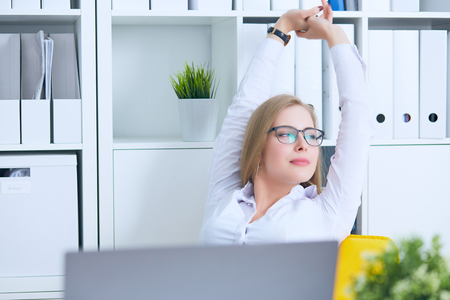 Young Caucasian business woman is relaxing at work holding hands behind head.の写真素材
