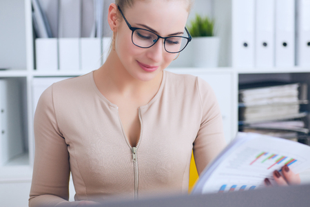 Young beautiful Caucasian businesswoman in glasses working on notebook computer and business document at office.の写真素材