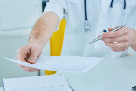 Middle section of a male medicine doctor holding and giving medical form and pen to patient closeup.の写真素材