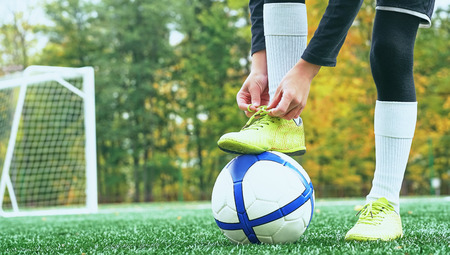 Boy football soccer tying the laces on the boots on grassy football stadium.の写真素材