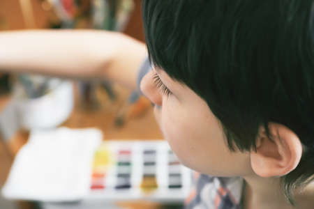 Young boy sitting in front of easel painting a fish, holding a brush in hand. Boy is getting ready to become an artist.の写真素材