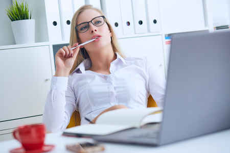 Young Caucasian business woman in glasses looks thoughtfully into the distance holding the pen in her mouth and thinks.の写真素材