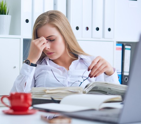 Tired Caucasian businesswoman holding eyeglasses and massaging nose bridge. Girl feeling discomfort from long wearing glasses at workplace.の写真素材