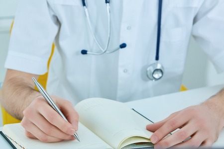 Male doctor or medical student holding ballpoint pen and writing on notepad. Therapist fills the patient admission scheduleの写真素材