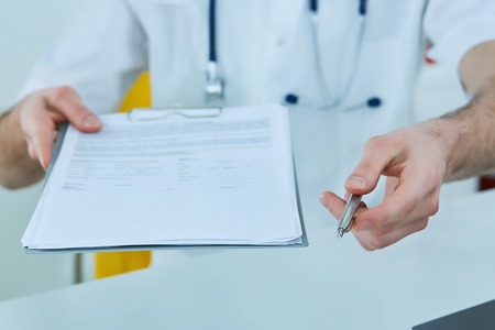 Middle section of a male medicine doctor holding and giving medical form and pen to patient closeup.の写真素材