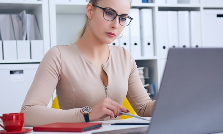 Young beauiful Caucasian businesswoman in glasses working on notebook computer and business document at office.の写真素材