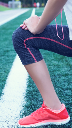 Young fitness girl doing stretching on the stadium. Summer sport activity. Green stadium grass on background.の写真素材