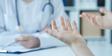 Young woman consulting with medical doctorcomplaining about health, having problems. Focus on patients hands. Private health care facility reception, admission complaints.の写真素材
