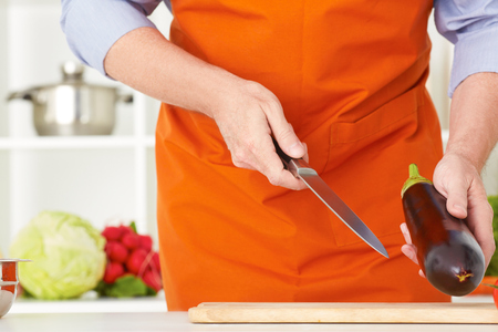 Closeup mature mans hands cutting vegetables on a work surface in a kitchen.の写真素材
