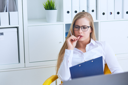 Young beauiful Caucasian businesswoman in glasses intently working on notebook computer and business document at office.の写真素材
