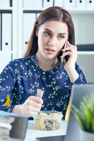 Business woman eating lunch at her workplace looking at the laptop screen. Folders with documents in the foreground. Dedline concept.の写真素材