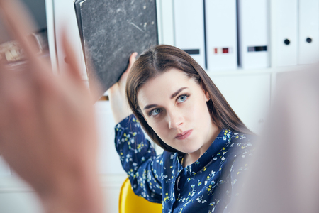 Angry business woman with folder trying to hit his colleague in office. Stressful situations at work.の写真素材