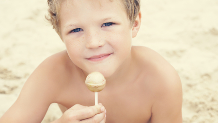Happy little preschool boy with candy lollypop at summer beach, outdoors.の写真素材